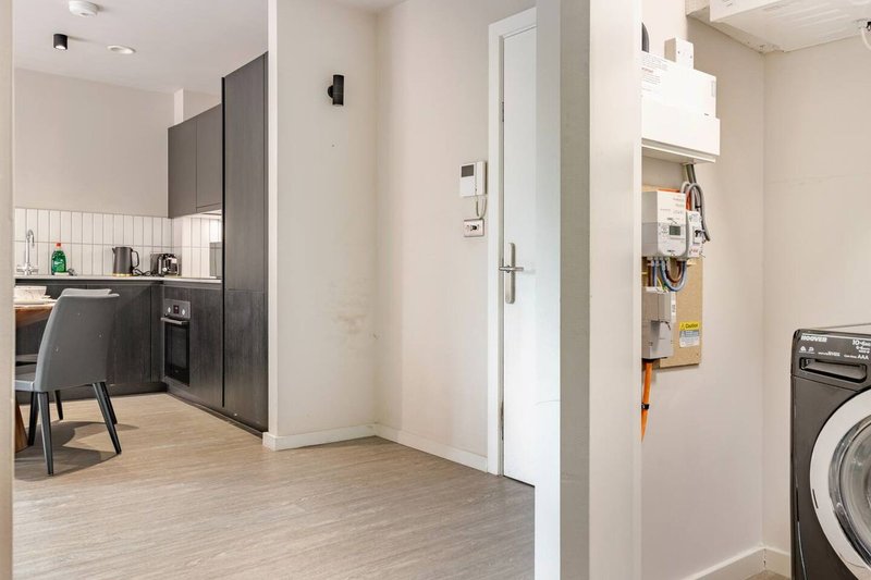 Modern kitchen and utility room with dark cabinetry, wooden flooring, washing machine and appliances