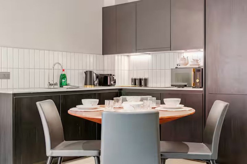 Modern kitchen with dining table, two chairs, white tile backsplash and grey cabinetry