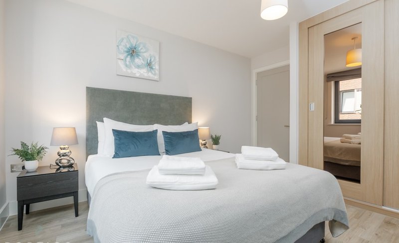 Modern bedroom with double bed, green headboard, blue pillows, white bedding and side table