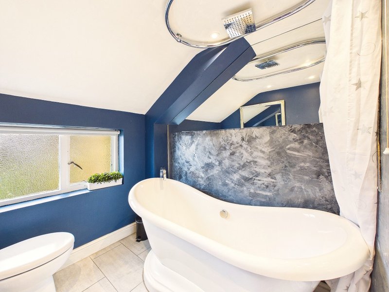 Modern bathroom with freestanding white bathtub, navy blue walls, window and toilet