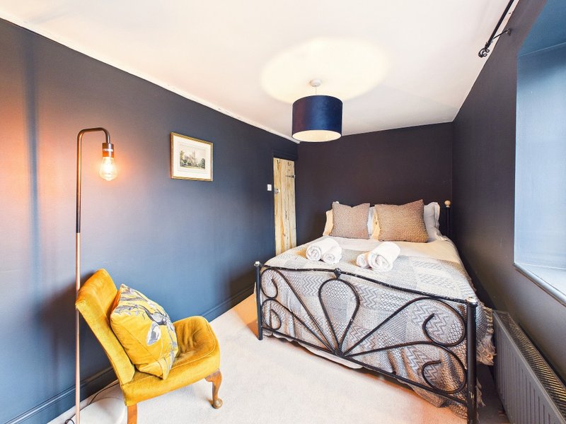 Bedroom with dark blue walls, metal bed frame, yellow armchair, and pendant lamp
