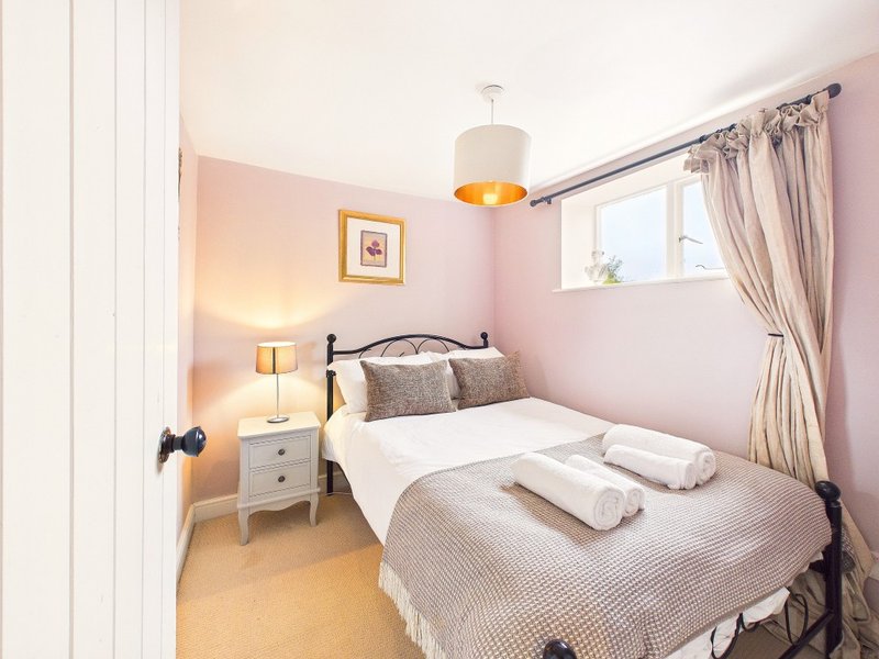 Pink bedroom with double bed, bedside lamp, white nightstand and window with curtains