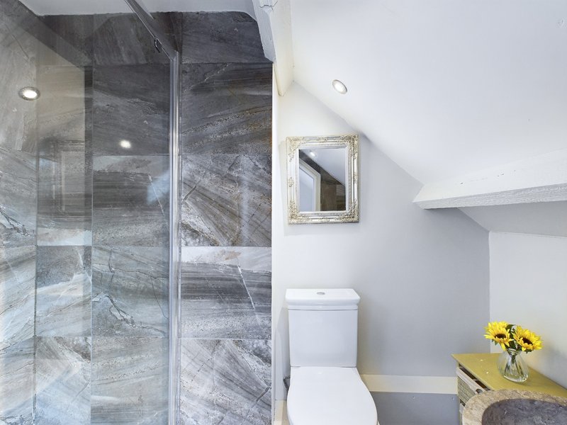 Modern bathroom with gray marble shower enclosure, white toilet, and yellow flowers on counter