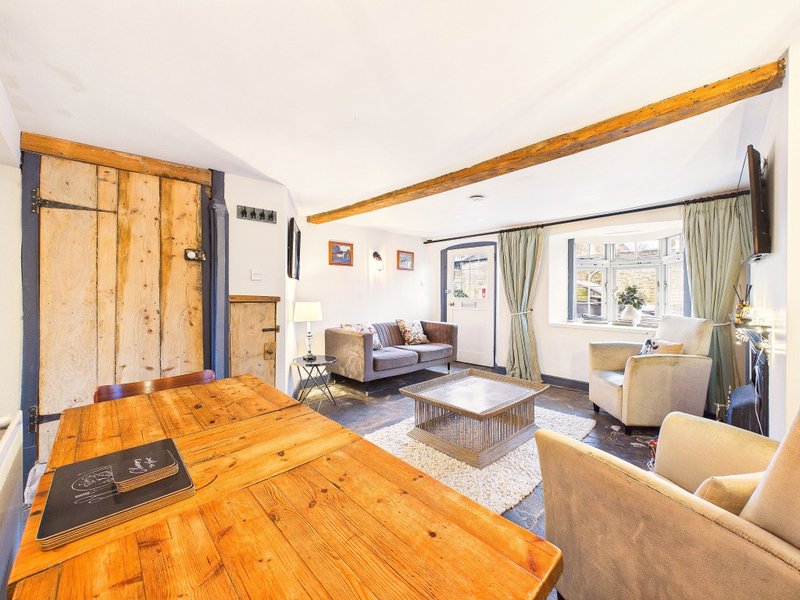Open-plan living space with wooden dining table, exposed beams, sofa, and large windows