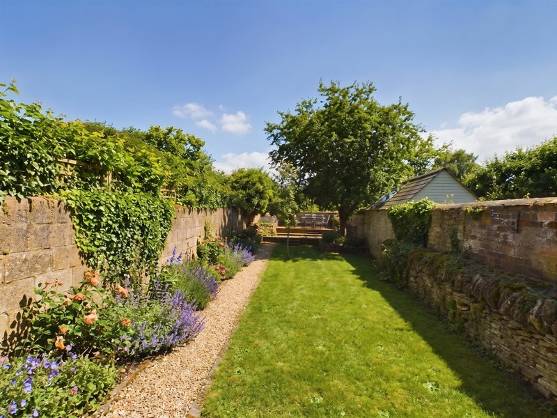 Garden pathway with stone walls, flowering plants, lawn, and trees