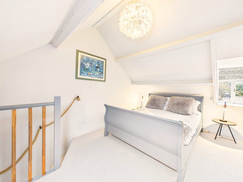 Bright attic bedroom with double bed, pendant light, framed artwork and wooden stair railing