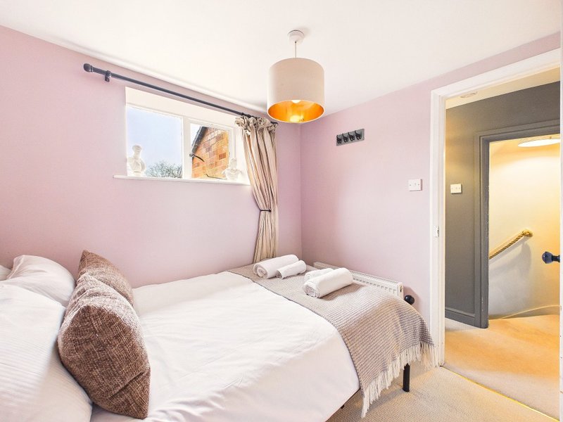 Pink bedroom with double bed, white bedding, pendant lamp and ensuite bathroom access
