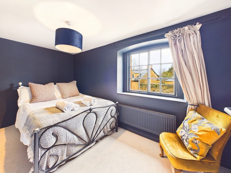 Bedroom with navy walls, metal-framed bed, yellow armchair and window with countryside view