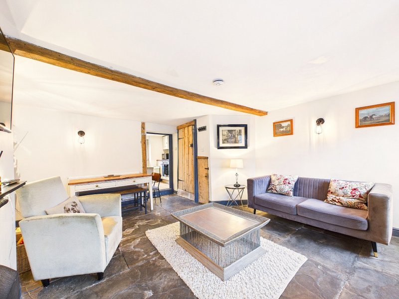 Open-plan living room with exposed beam, sofa, armchairs, coffee table and framed wall art
