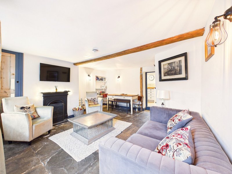 Open-plan living room with fireplace, sofas, TV, wooden beams and dining area
