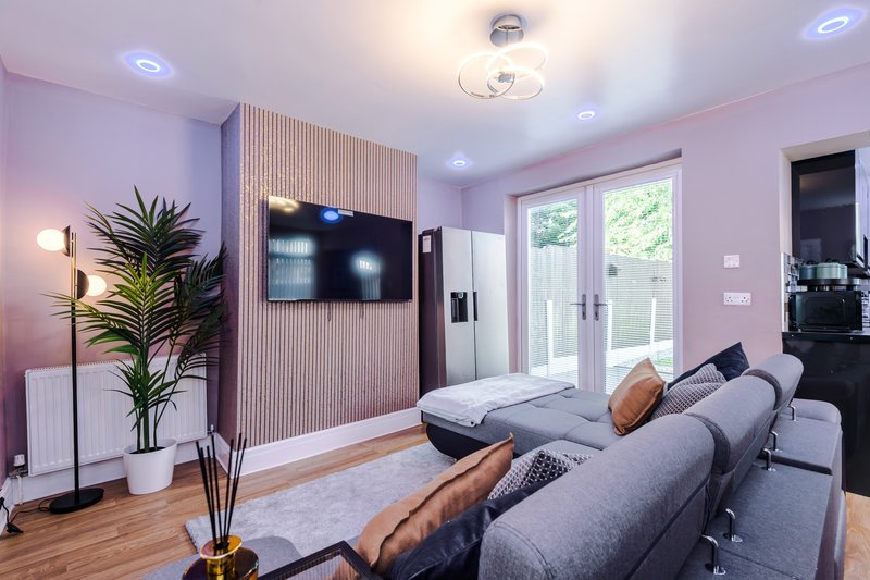 Modern living room with grey sofa, wall-mounted TV, potted plant and wooden flooring