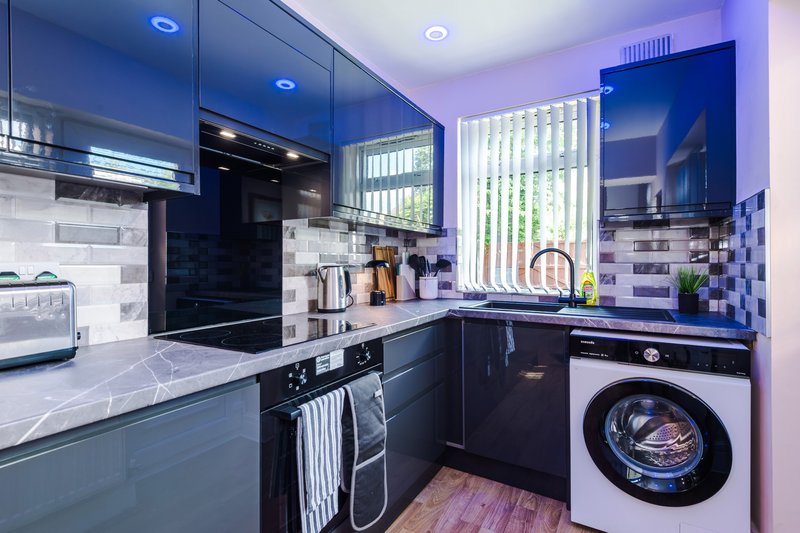 Modern kitchen with dark blue cabinets, white subway tile splashback, stainless steel appliances and washing machine
