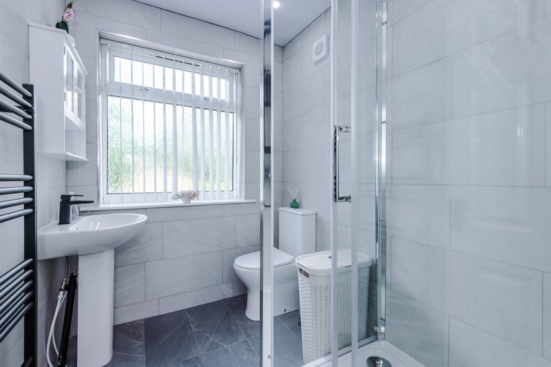 Modern bathroom with shower enclosure, pedestal sink, toilet and window