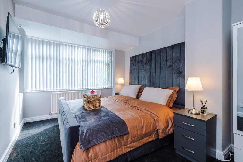 Modern bedroom with double bed, orange bedding, dark headboard, pendant light and bedside lamps