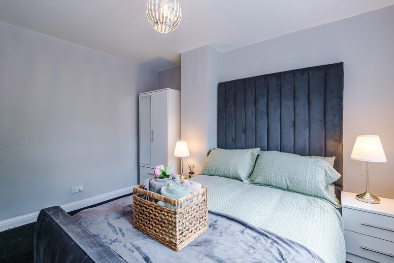 Modern bedroom with padded headboard, double bed with green pillows, bedside lamps and pendant light