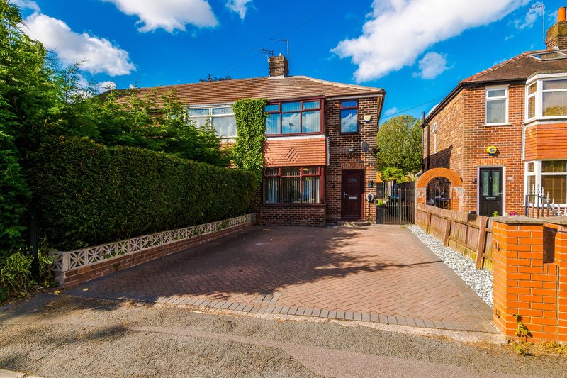 Brick semi-detached house with driveway, hedges, and clear blue sky