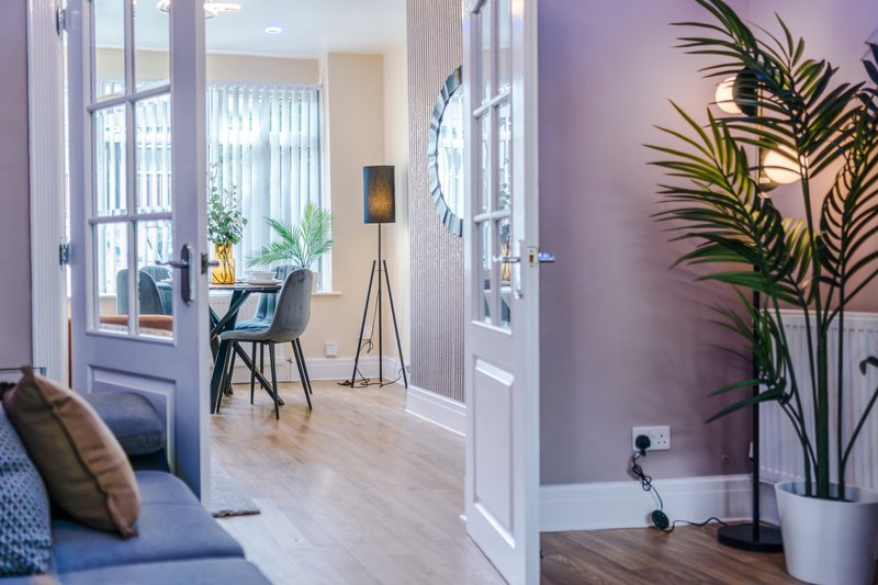 Modern living space with open-plan layout, purple accent wall, potted plants, and contemporary furniture