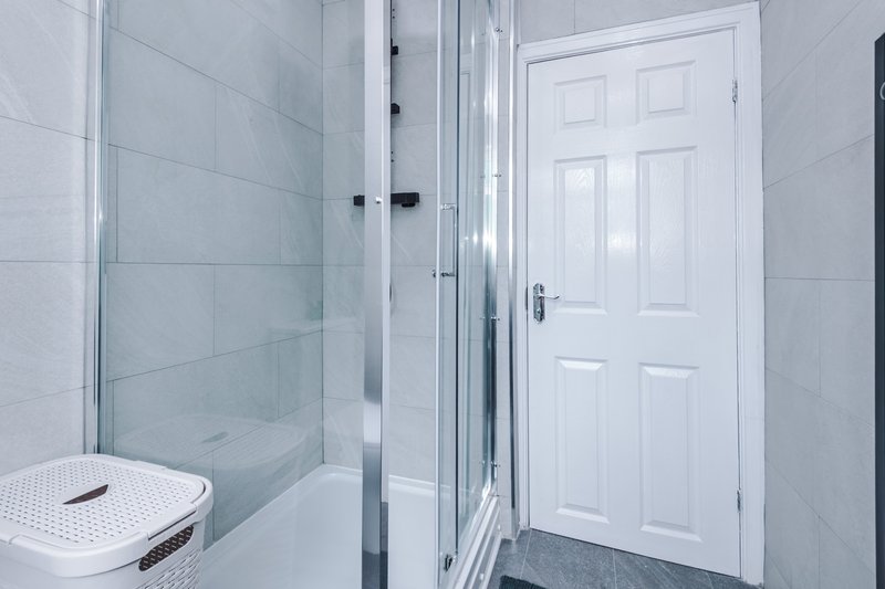Modern bathroom with walk-in shower, white door, and light grey tiling