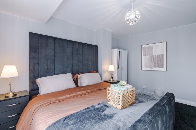 Modern bedroom with upholstered headboard, orange bedding, pendant light, and side lamps