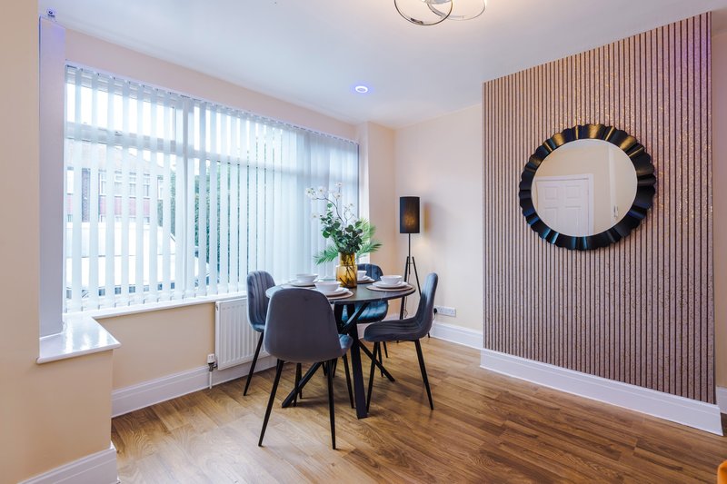Modern dining area with round table, black chairs, wall mirror and vertical wood paneling