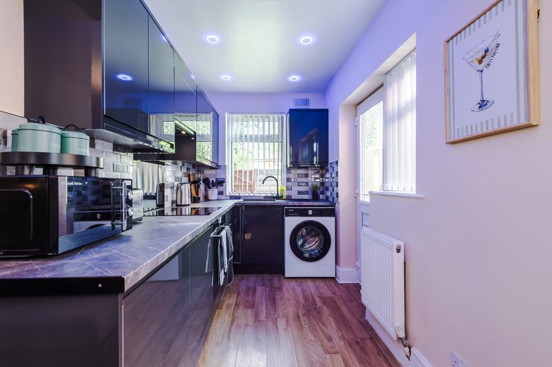 Modern kitchen with dark cabinets, marble countertop, stainless steel appliances and washing machine
