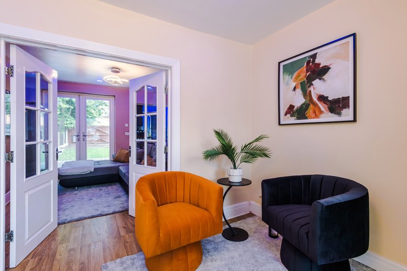 Living room with orange and black armchairs, small table, framed artwork, and open doors to garden room