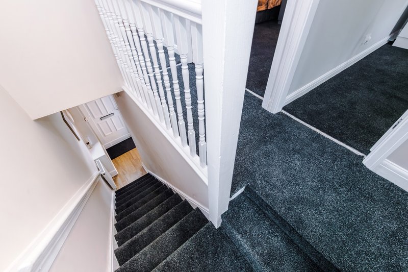 Staircase with black treads, white railings, and carpeted landing area