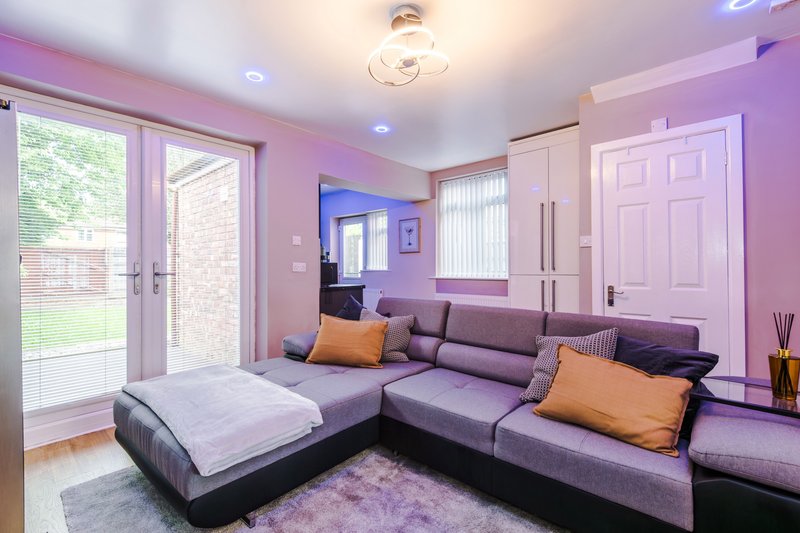 Modern living room with purple L-shaped sofa, orange cushions, garden views through patio doors