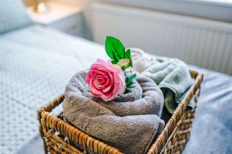 Wicker basket with folded towels and pink rose flower on bed