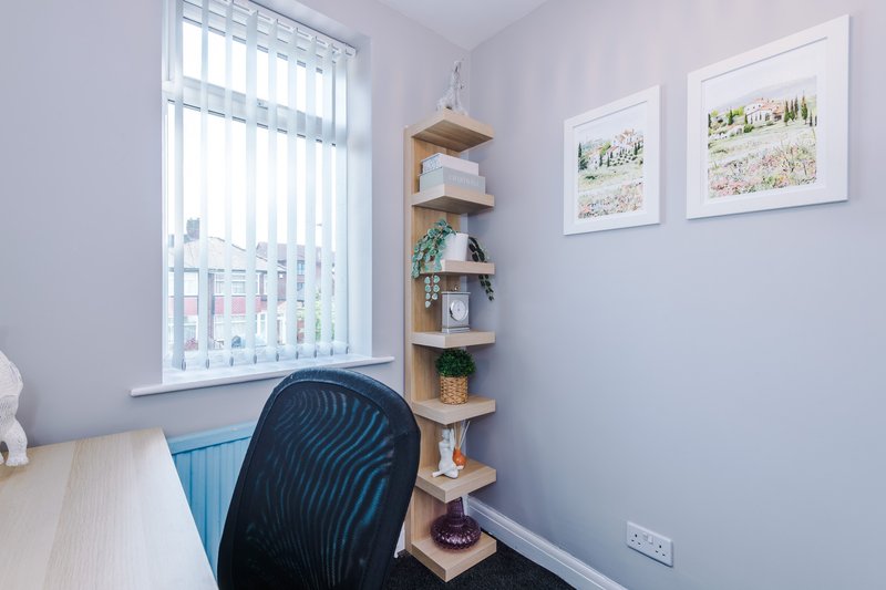 Bright office corner with desk, black chair, wooden corner shelves, and framed wall art