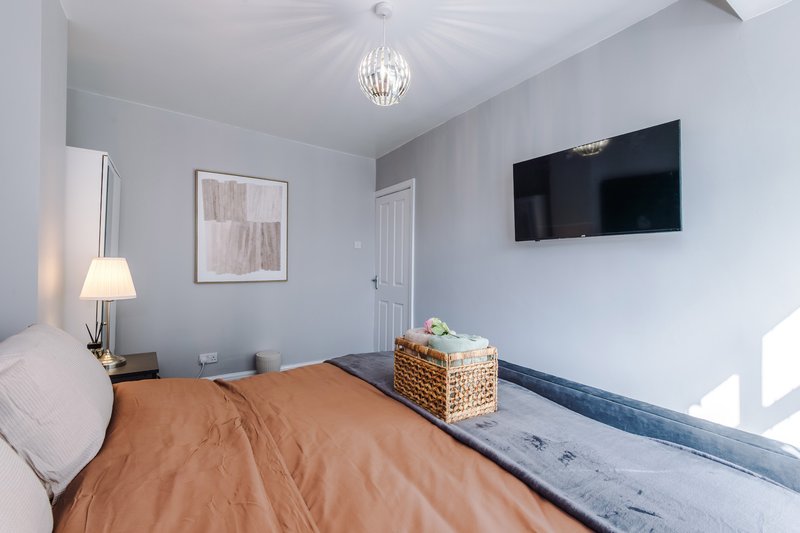 Modern bedroom with brown duvet, wall-mounted TV, pendant light and framed wall art