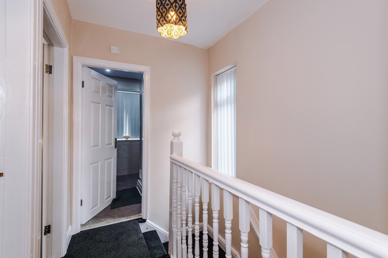 Hallway with staircase railing, pendant light fixture, and doorway to bathroom