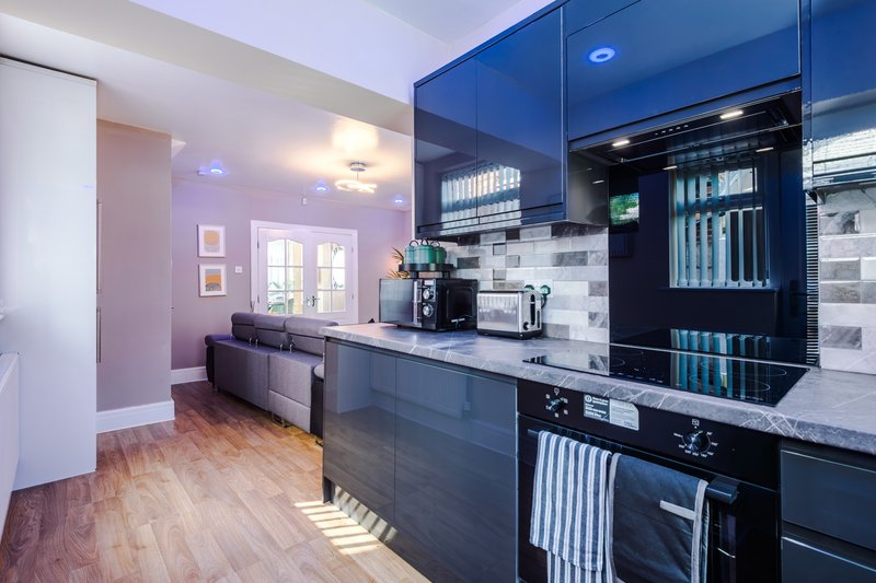Modern kitchen with blue cabinetry, white subway tile backsplash, wooden flooring and pink accent wall