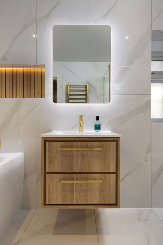 Modern bathroom with wall-mounted wooden vanity, illuminated mirror, and marble tile walls