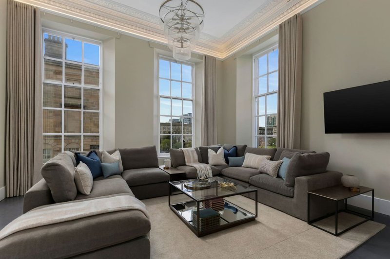 Bright living room with large windows, gray sectional sofa, black TV, and glass coffee table