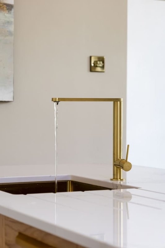 Modern kitchen sink with brass faucet and white countertop, minimalist design