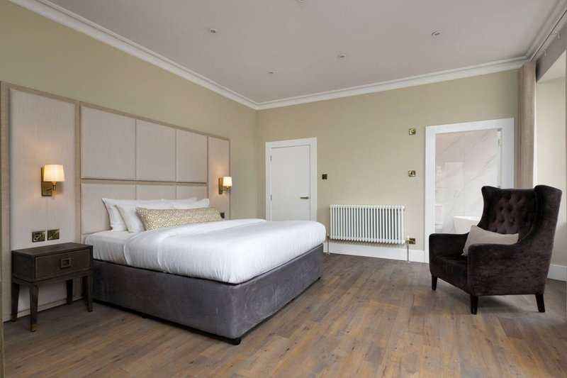 Spacious bedroom with double bed, upholstered headboard, wooden flooring and armchair