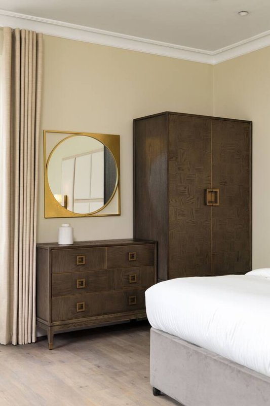 Bedroom with dark wood furniture, round mirror, cream curtains and white bed