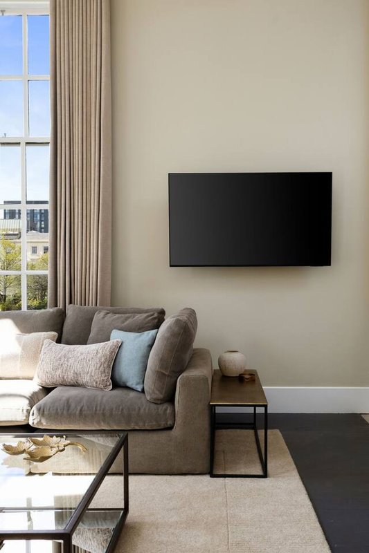 Modern living room with gray armchair, wall-mounted TV, window with curtains, and coffee table