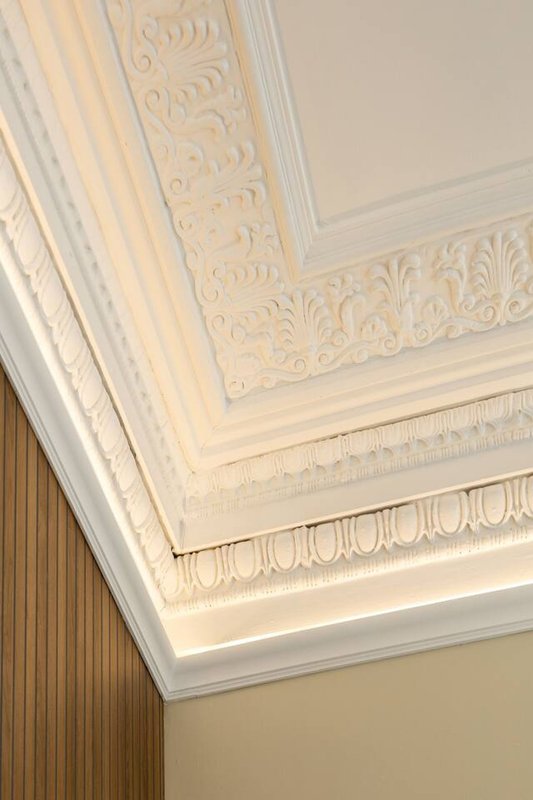 Ornate white ceiling cornice and decorative plasterwork detail with warm lighting