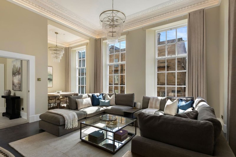 Spacious living room with grey sectional sofa, glass coffee table, large windows and pendant lighting