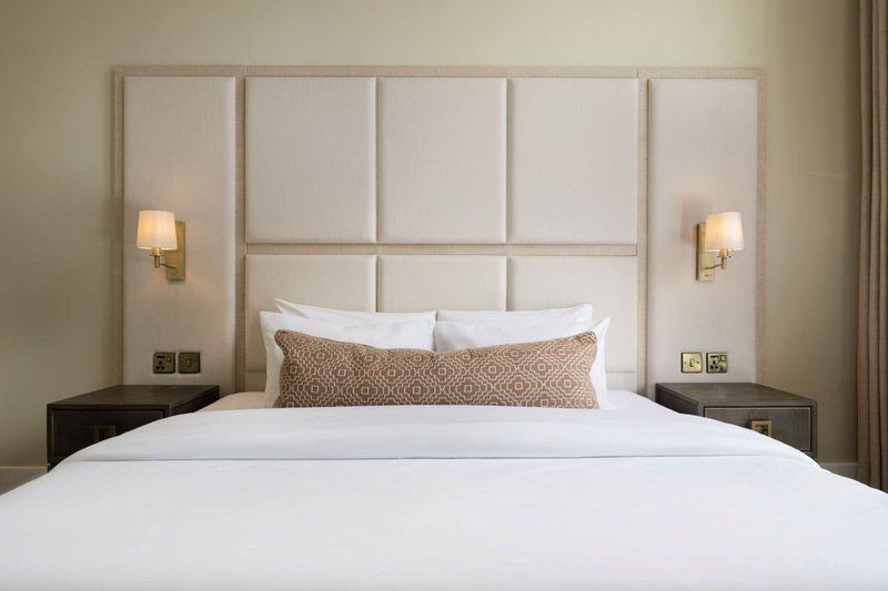 Modern bedroom with upholstered headboard, white bedding, patterned cushion and wall sconces