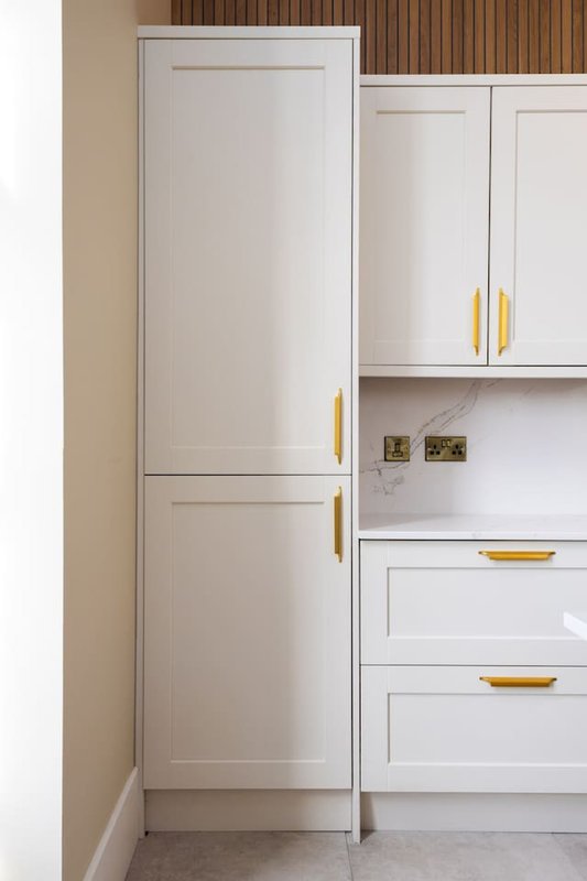 Modern kitchen with white cabinetry, gold handles, and wooden backsplash detail