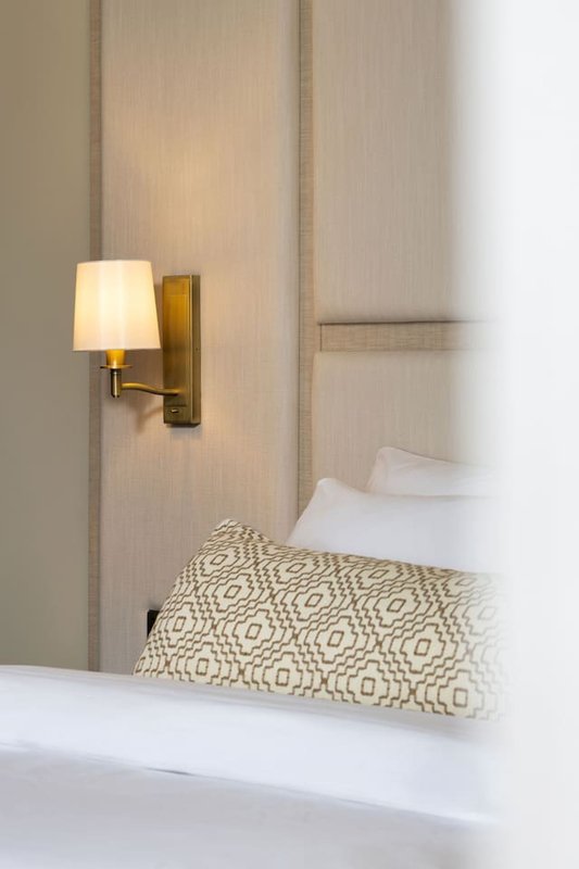 Bedroom alcove with wall-mounted brass lamp, patterned cushion and white bedding