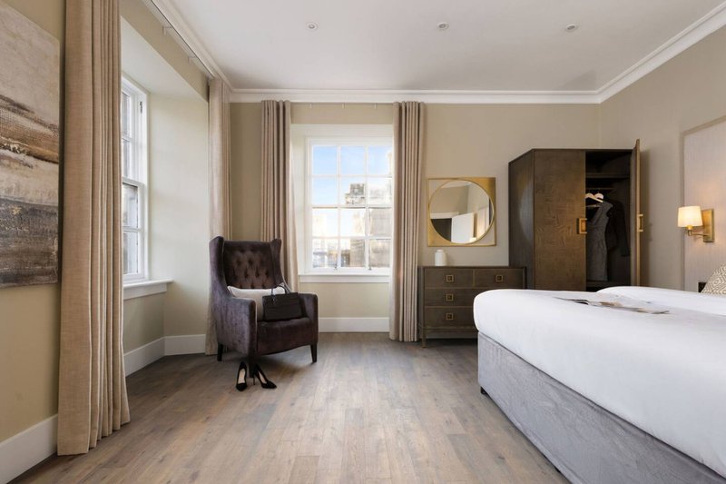 Spacious bedroom with double bed, armchair, wooden floor, and large window with city view