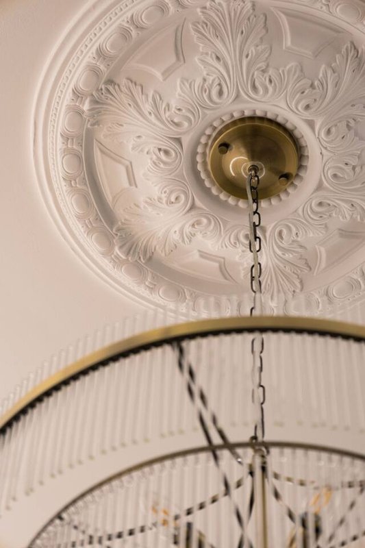 Ornate white ceiling rose with brass light fixture and decorative pendant chain