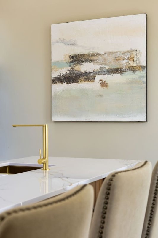 Modern kitchen or dining area with abstract artwork, brass tap, white countertop and upholstered chair