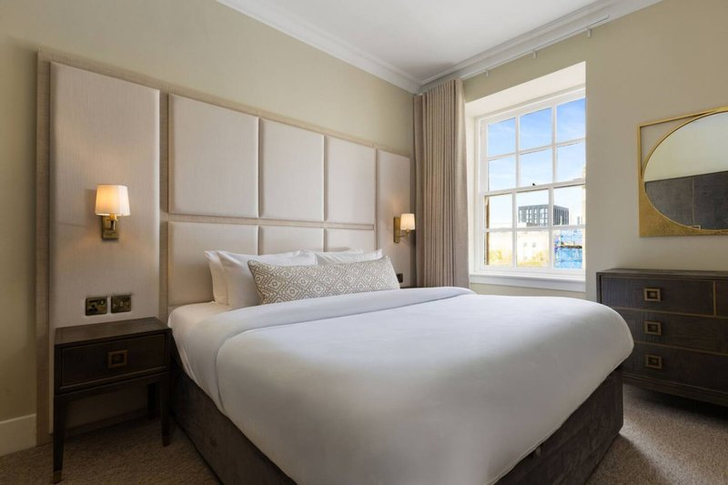 Modern bedroom with double bed, upholstered headboard, dark wood nightstands, and large window with city view