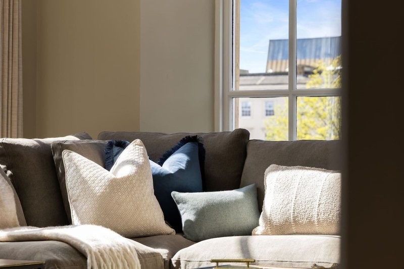 Living room with grey sofa, decorative cushions, and large window overlooking residential street