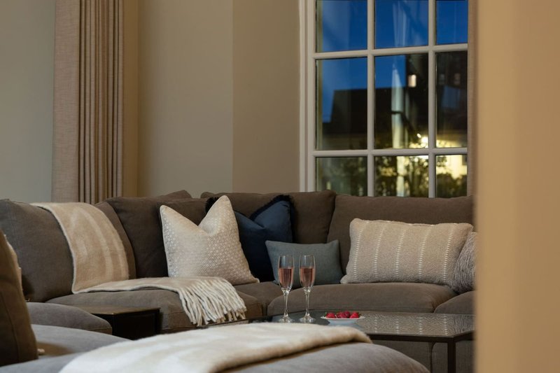 Modern living room with gray corner sofa, decorative cushions, throw blanket, and large window at dusk